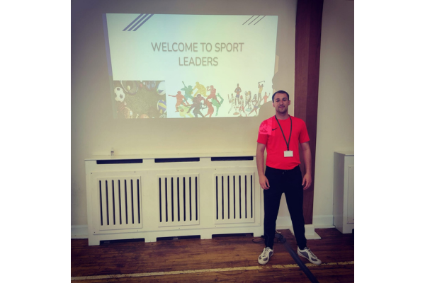 Dan stands in front of a "welcome to sport leaders" presentation