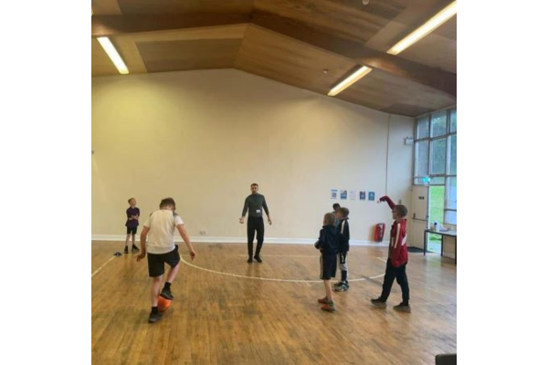 Dan stands in a hall with a group of young boys playing football
