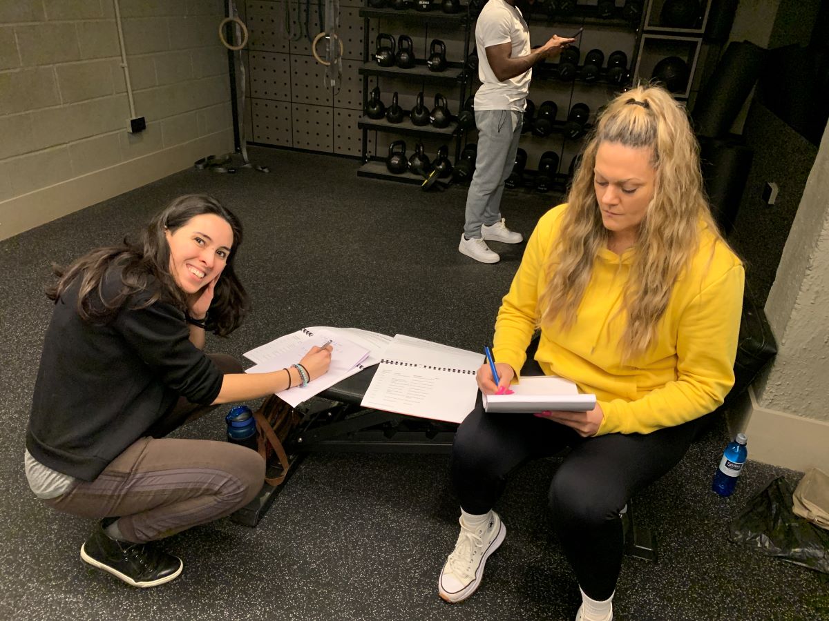 Two women sat in a gym writing notes