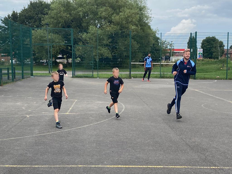 A group of children running with a coach on a tarmac court
