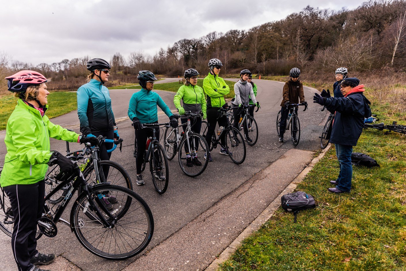 A group of cyclists listening to an instructor at the side of a road