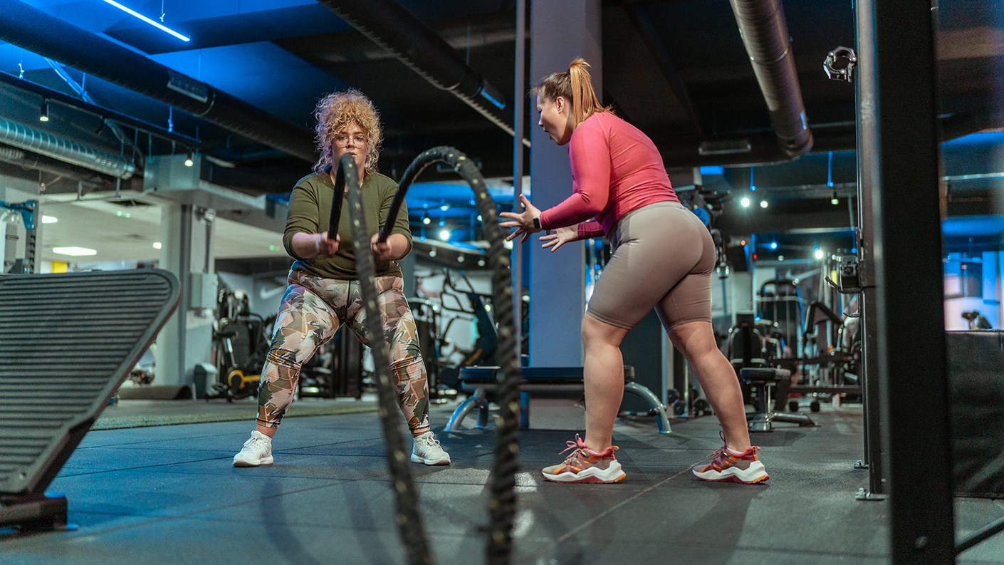 Gym rope session with personal trainer encouraging woman