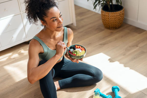 Woman sitting on floor eating a bowl of fruit