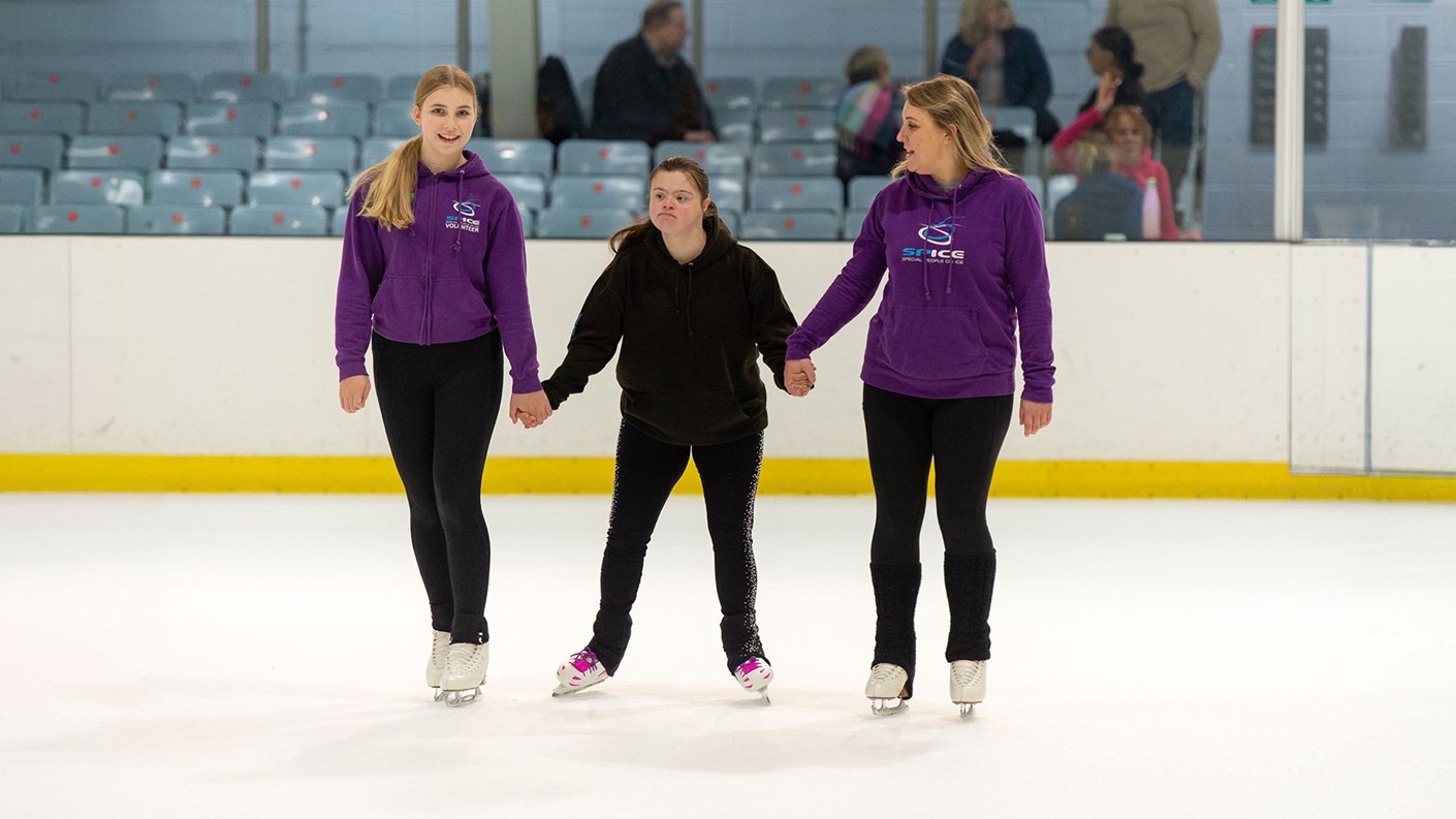 Two skating coaches teaching a skater with Down's Syndrome