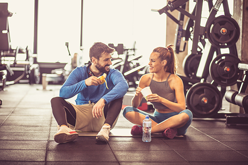 Two people in gym clothes sat down eating nutritional food at a gym