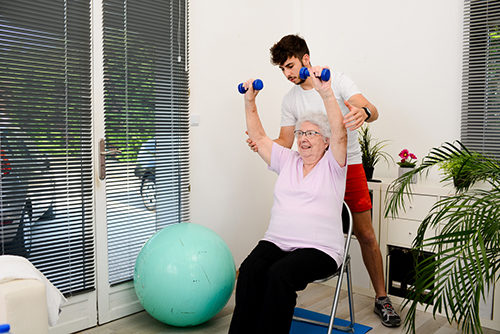 A personal trainer helping a seated older lady lifting weights