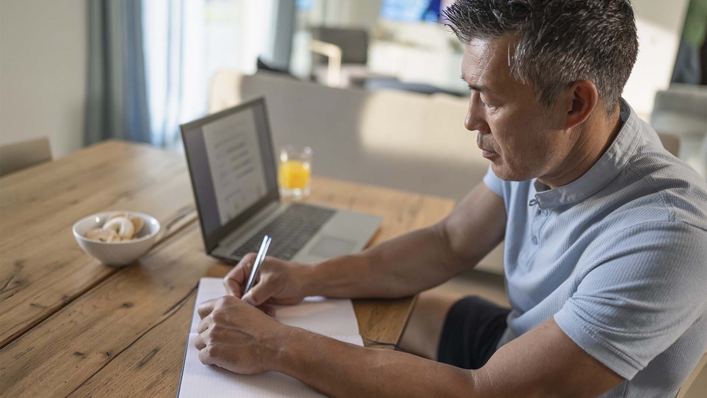 Man taking notes as he takes part in a webinar