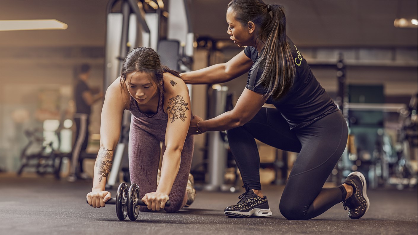 Female personal trainer working to help female client with exercise wheel