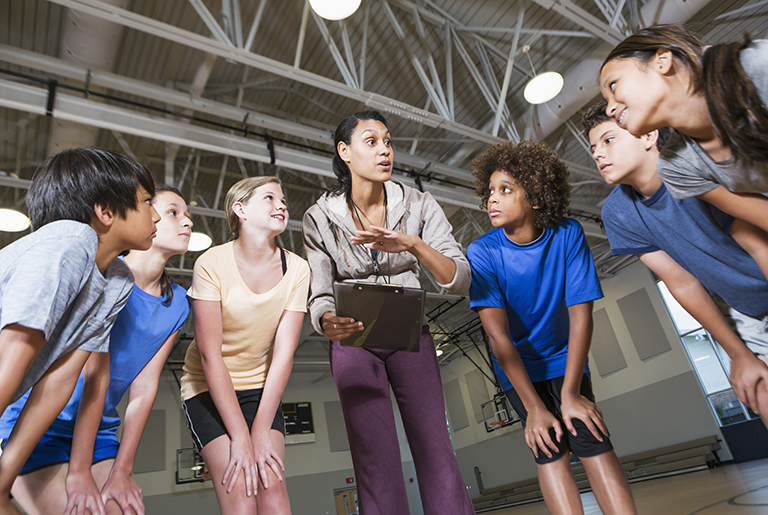 Teacher or coach taking to their students in a crouched circle/huddle.