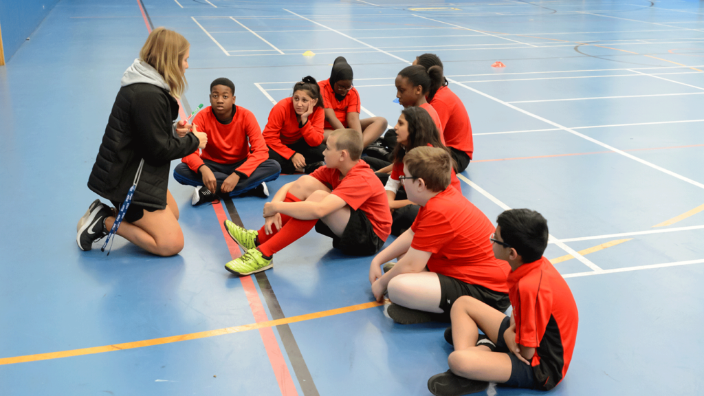 Coach with teenagers sitting down in sports hall